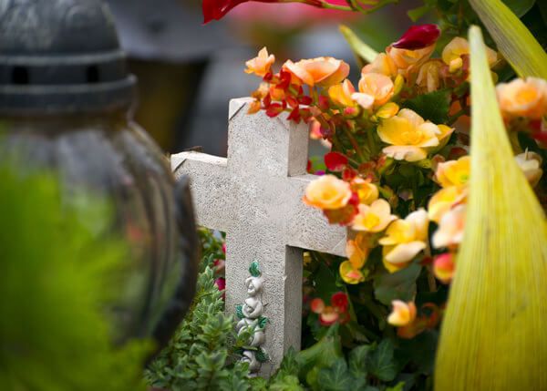 Steinkreuz umringt von Blumen - auf dem Friedhof